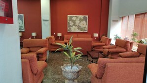 A lobby with red walls, multiple orange sofas arranged in a semi-circle, a central decorative plant, and a large floral painting on the wall. - Romantic Apartment in Sevilla Near Giralda (Seville)