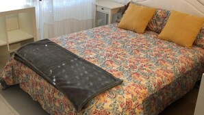 A bed with a patterned bedspread and two pillows, a bedside table, a lamp, and a window with sheer curtains. - Romantic Apartment in Sevilla Near Giralda (Seville)