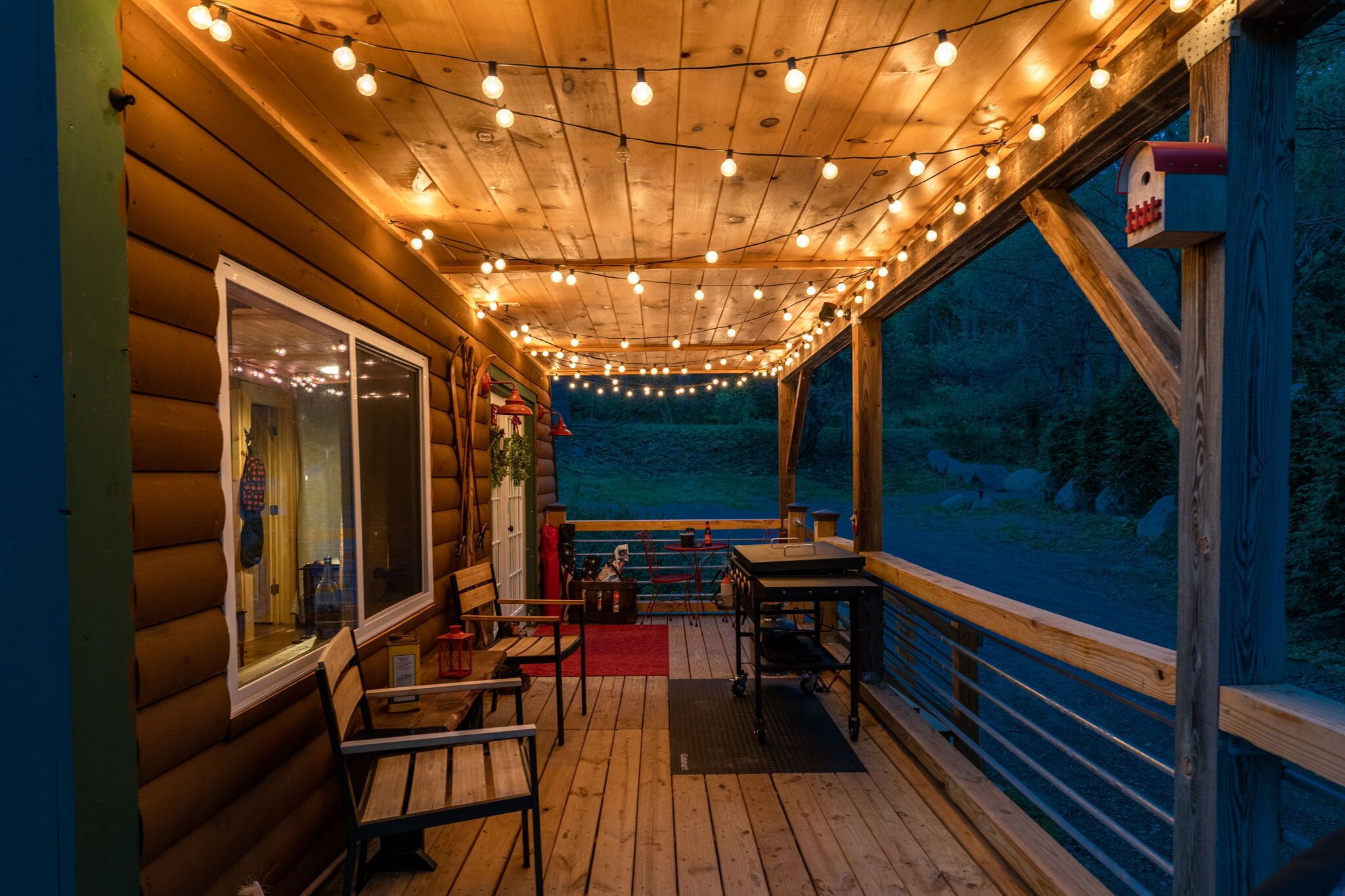 Una terraza de madera con luces, una mesa, sillas y vistas al bosque.