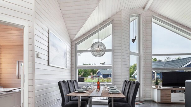 A dining area with a table set for four, large windows, and a hanging light fixture. - Vacation home with trampoline, sauna & fireplace - up to 3 dogs - fully fenced (Schönberg (Holstein))