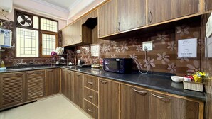 A kitchen with wooden cabinets, a microwave, and a window with a fan. - Irra Homes • 2BHK Apartment • Panoramic Valley View (Shimla)