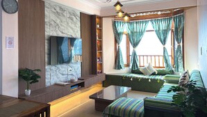 A modern living room with a flat-screen TV, a sofa, a coffee table, and a dining area with a wooden table and chairs. - Irra Homes • 2BHK Apartment • Panoramic Valley View (Shimla)