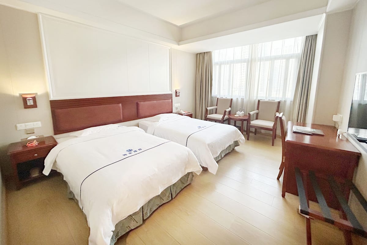 Une chambre d’hôtel avec deux lits, un bureau, une chaise et un téléviseur.