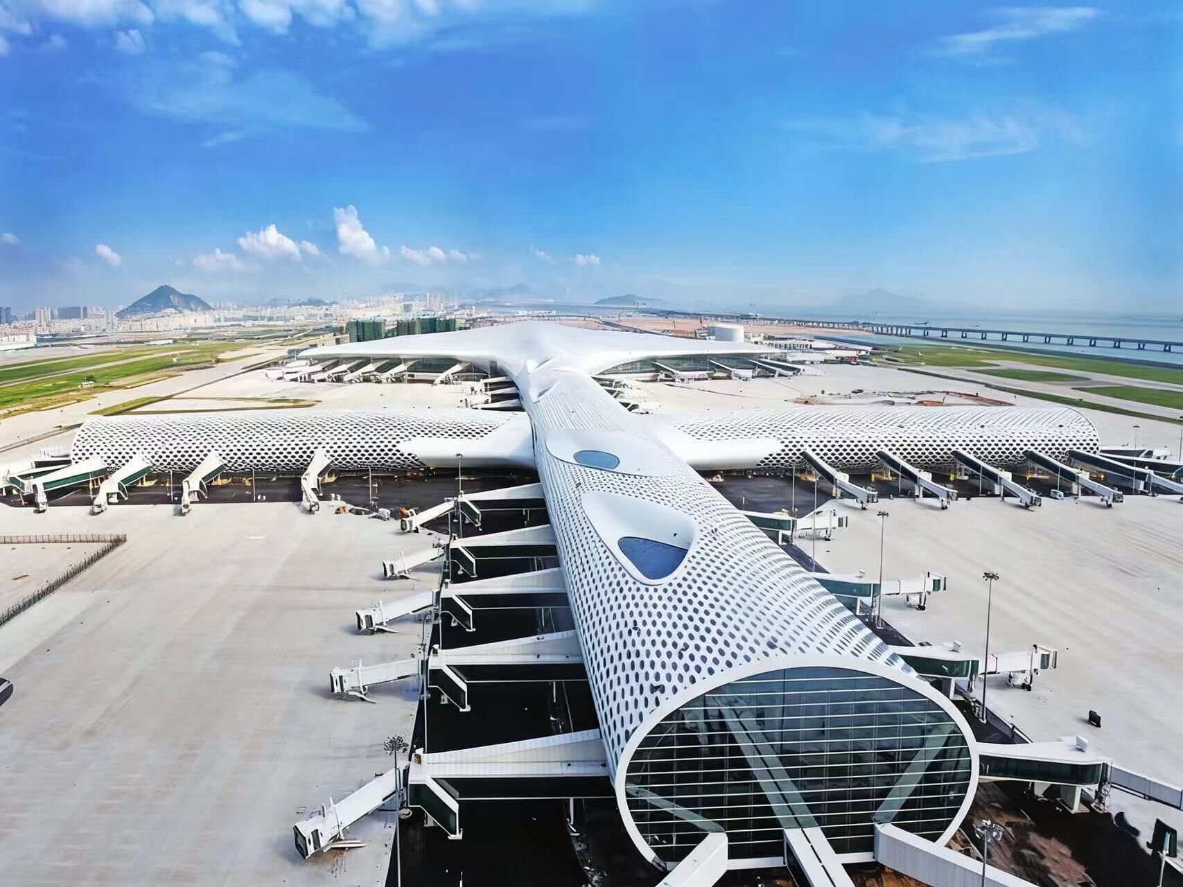 Un terminal d’aéroport moderne, doté d’un toit incurvé original, de plusieurs passerelles d’embarquement et offrant une vue sur le paysage urbain en arrière-plan.