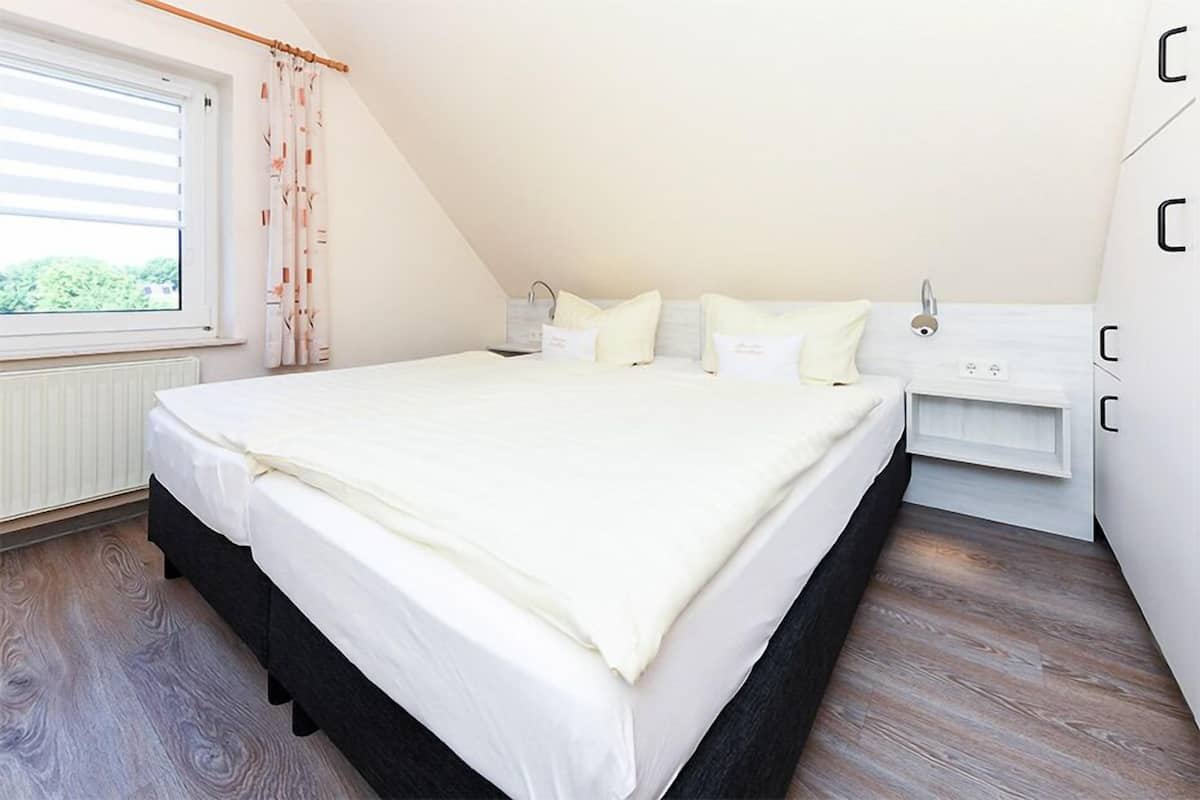 A bedroom with a large bed, a window with blinds, a radiator, and a wardrobe.