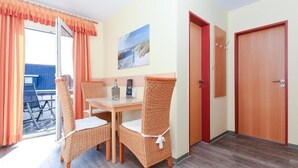 A room with a dining table, wicker chairs, a painting on the wall, and a door.