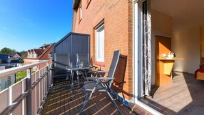 A balcony with a table and chairs, a sliding door, and a view of neighboring houses.