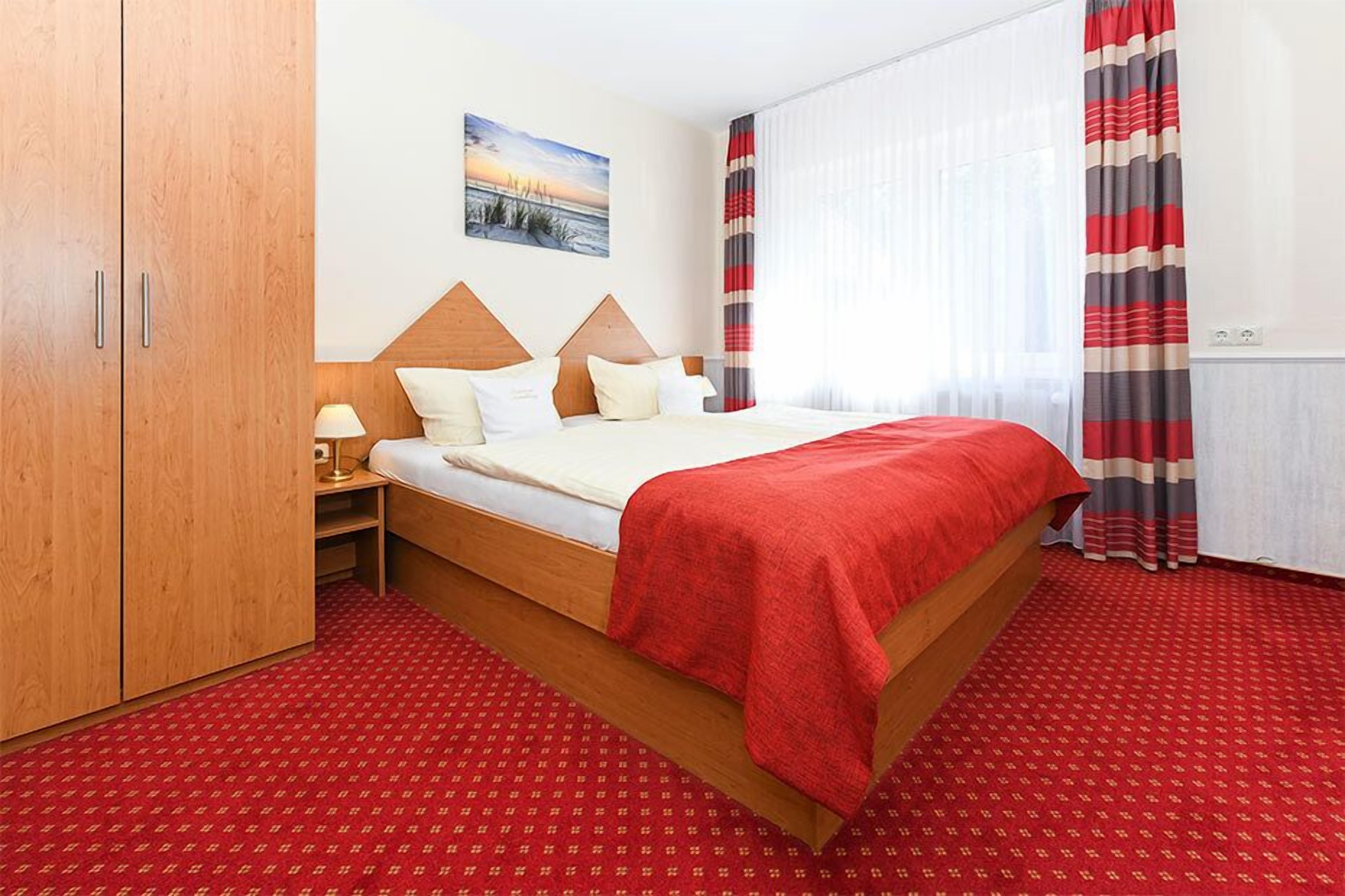 A hotel room with a bed, a nightstand, a lamp, a painting, and striped curtains.