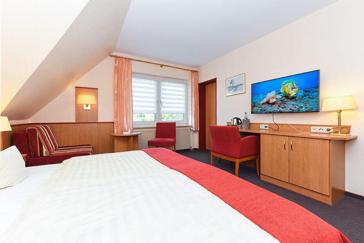 A hotel room with a bed, a desk, a chair, a television, and a window with curtains.