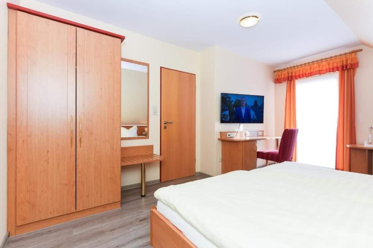 A hotel room with a bed, a desk with a chair, a TV, and a wardrobe.
