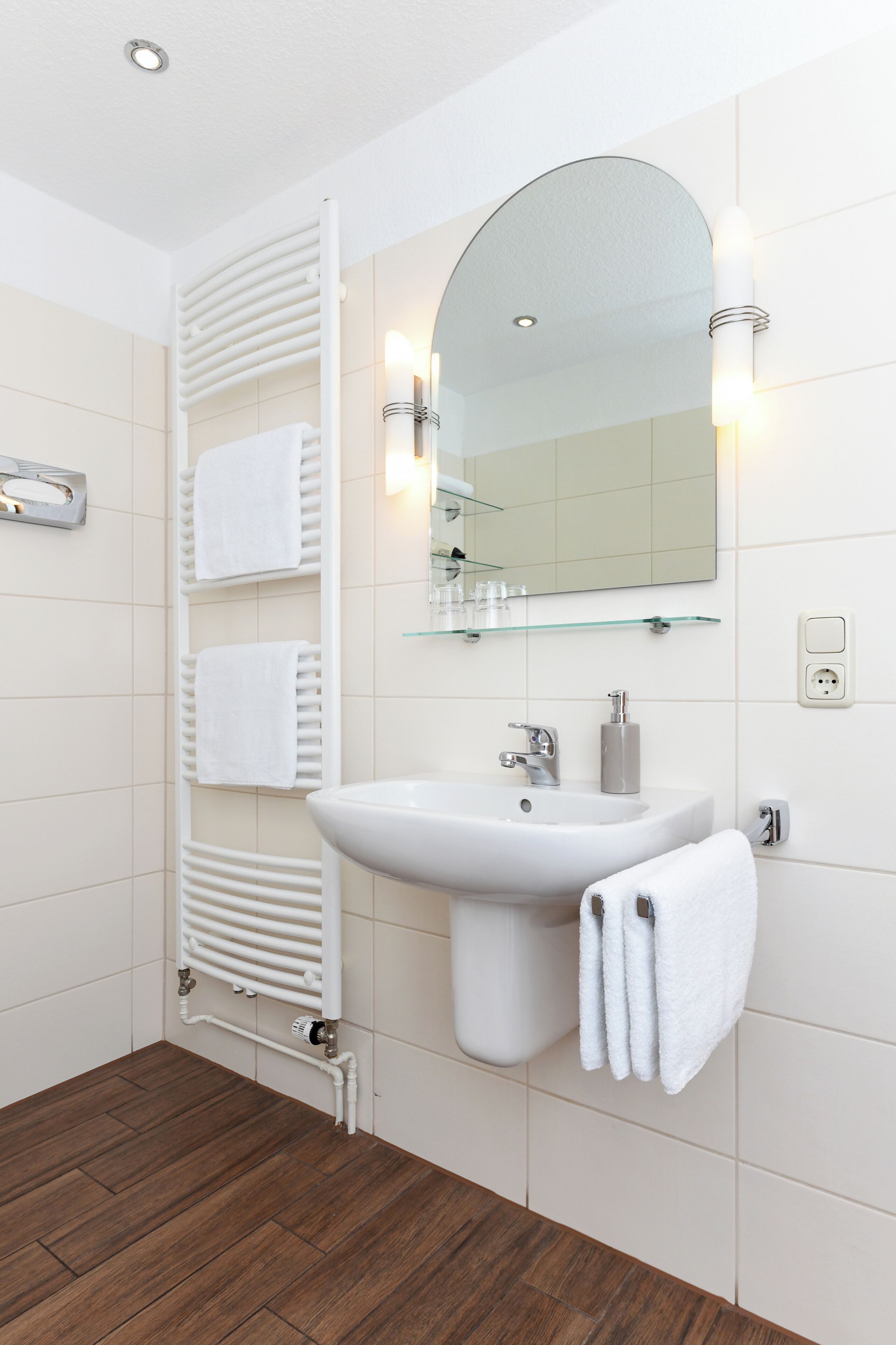 A modern bathroom with a white sink, mirror, towel rack, and heated floor.