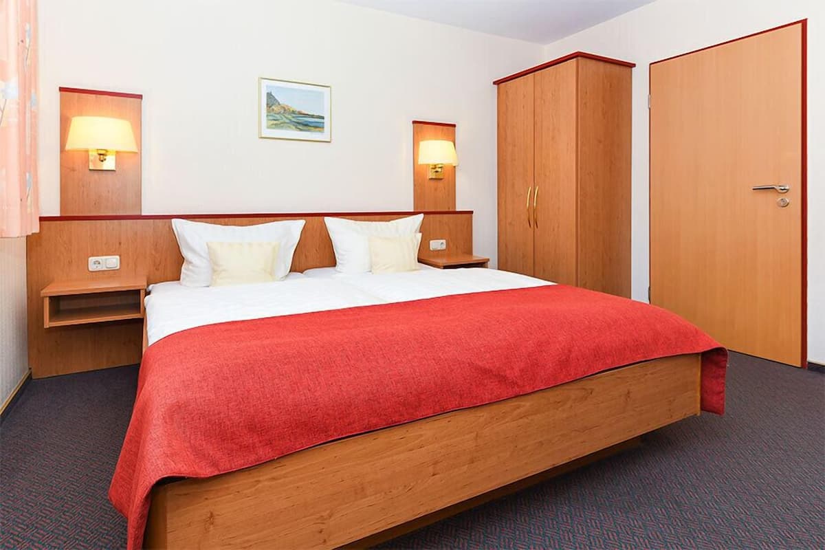 A hotel room with a bed, two bedside lamps, a nightstand, a wardrobe, and a wall-mounted picture.