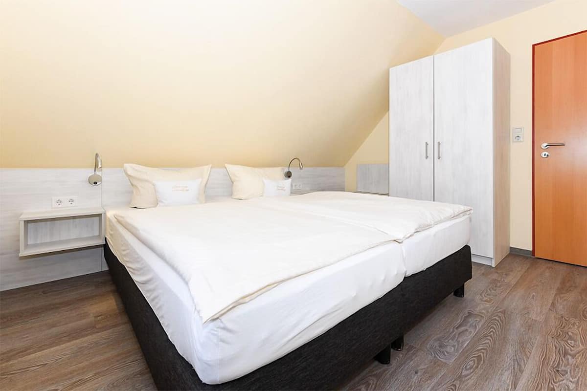 A bedroom with a large bed, a wardrobe, and a wooden floor.