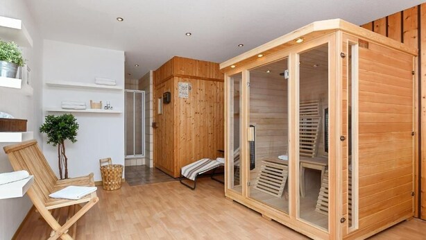 A wooden sauna with glass doors, a wooden bench, a small plant, and a white shelf with towels.