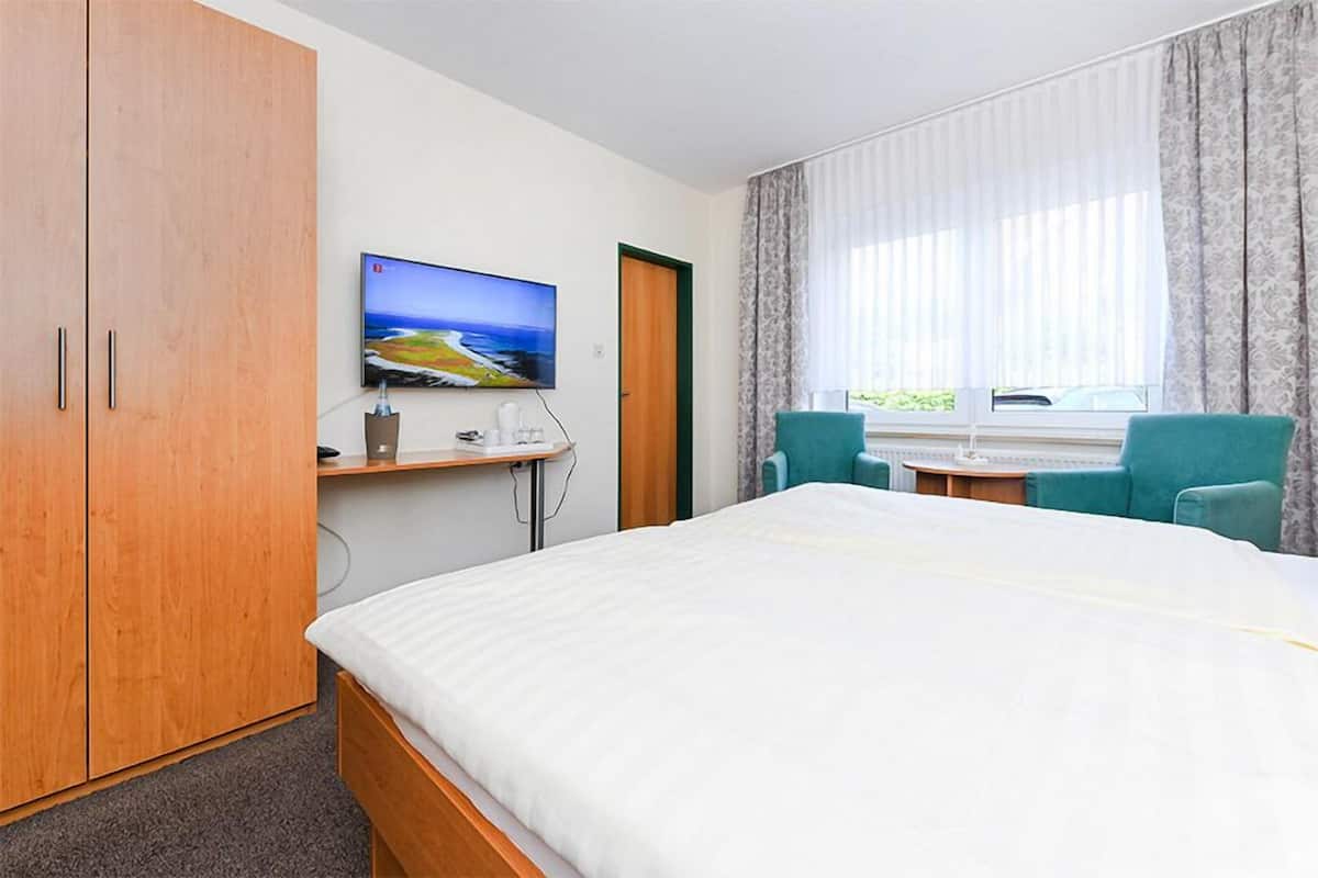 A hotel room with a bed, a TV, a desk with a chair, and a window with curtains.