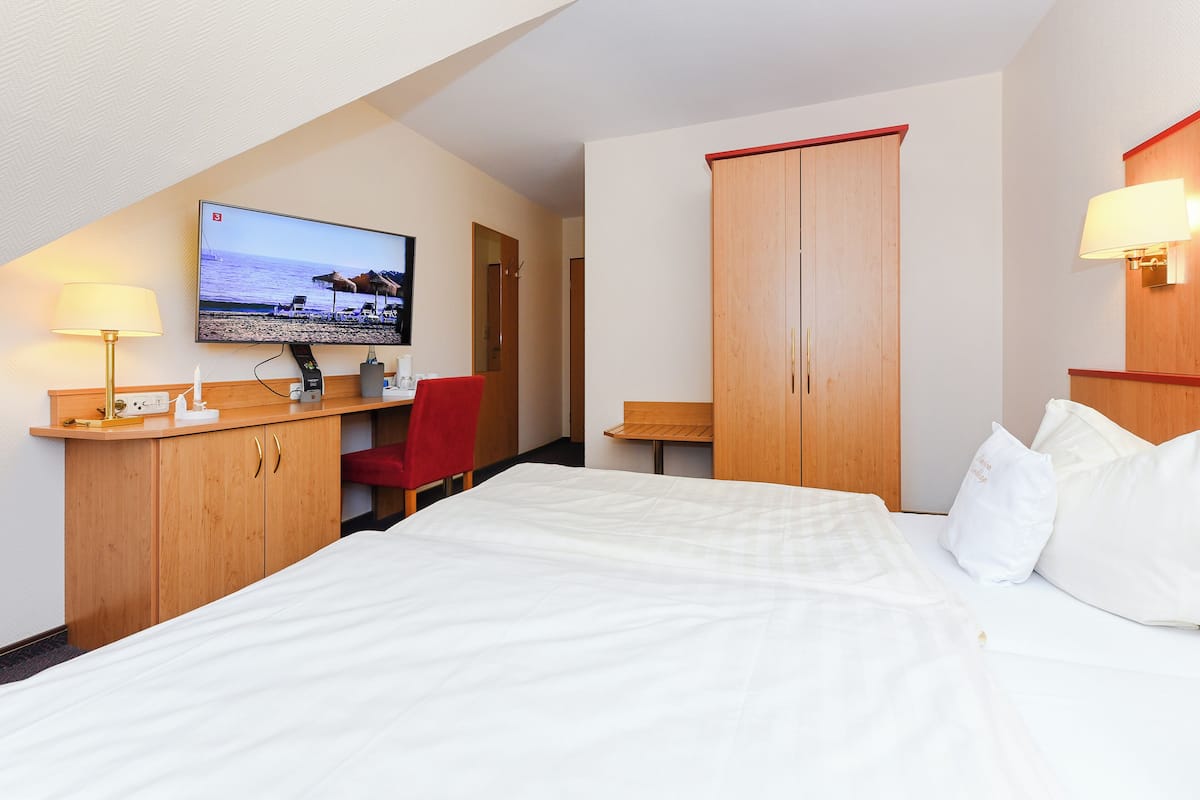 A hotel room with a bed, a desk with a computer, a TV, and a wardrobe.