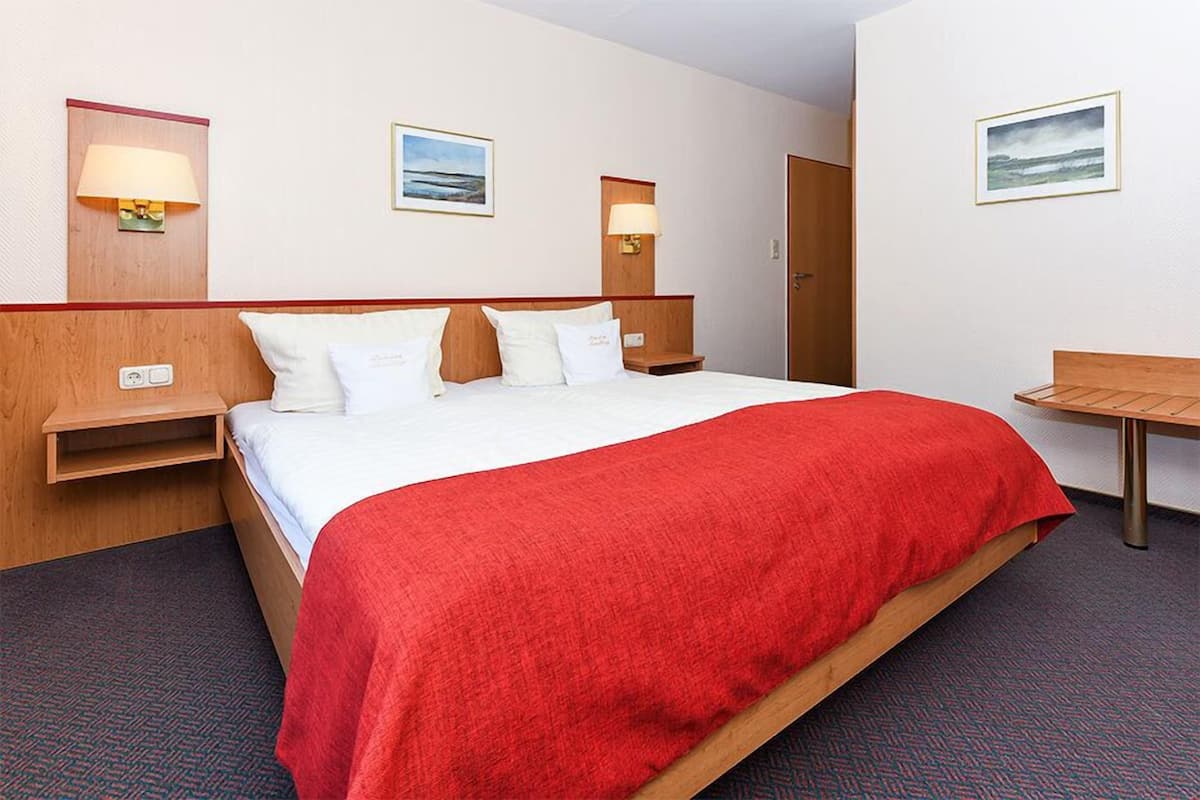 A hotel room with a bed, bedside tables, a desk, and wall-mounted lamps.