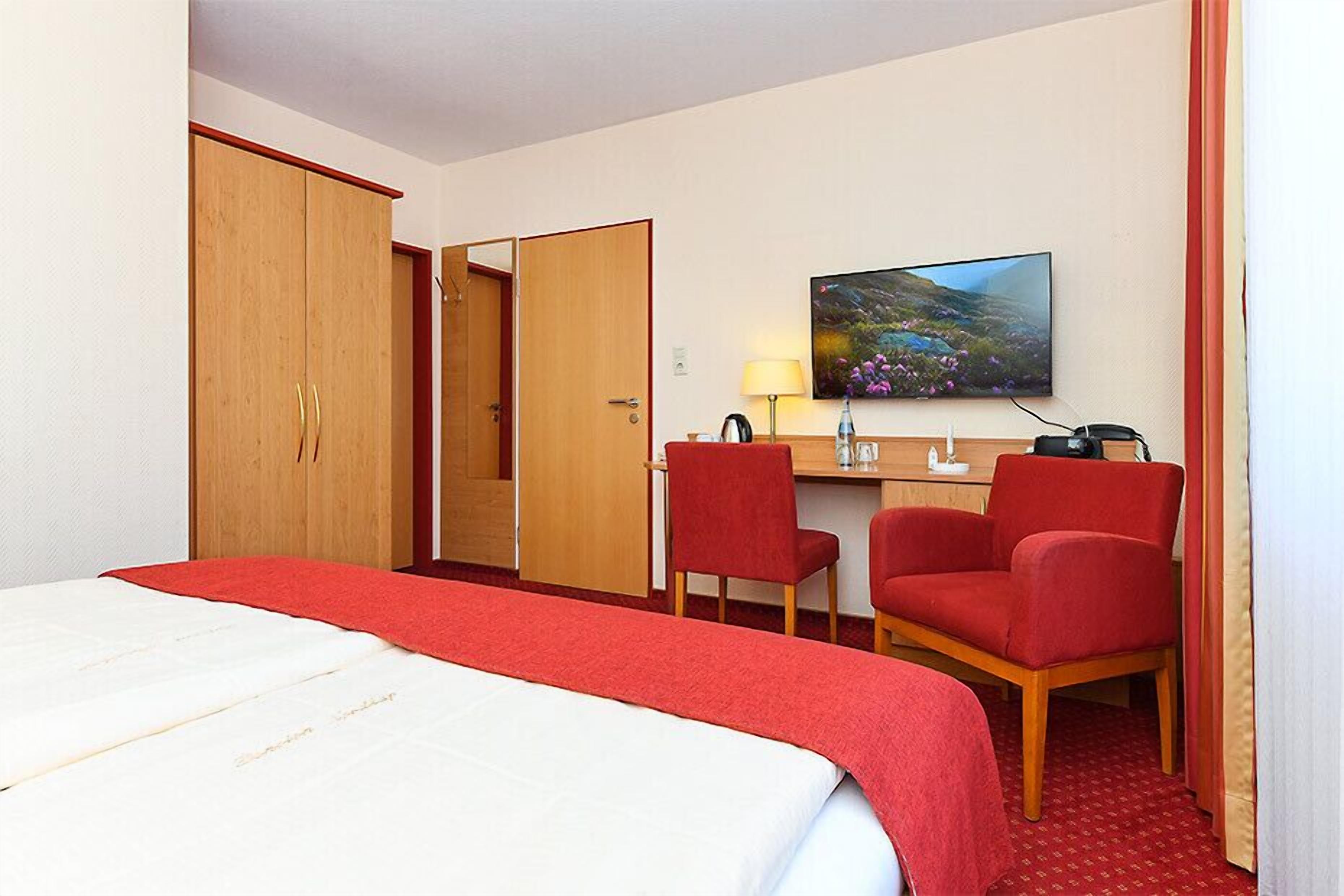 A hotel room with a bed, a desk, two chairs, a TV, and a painting on the wall.