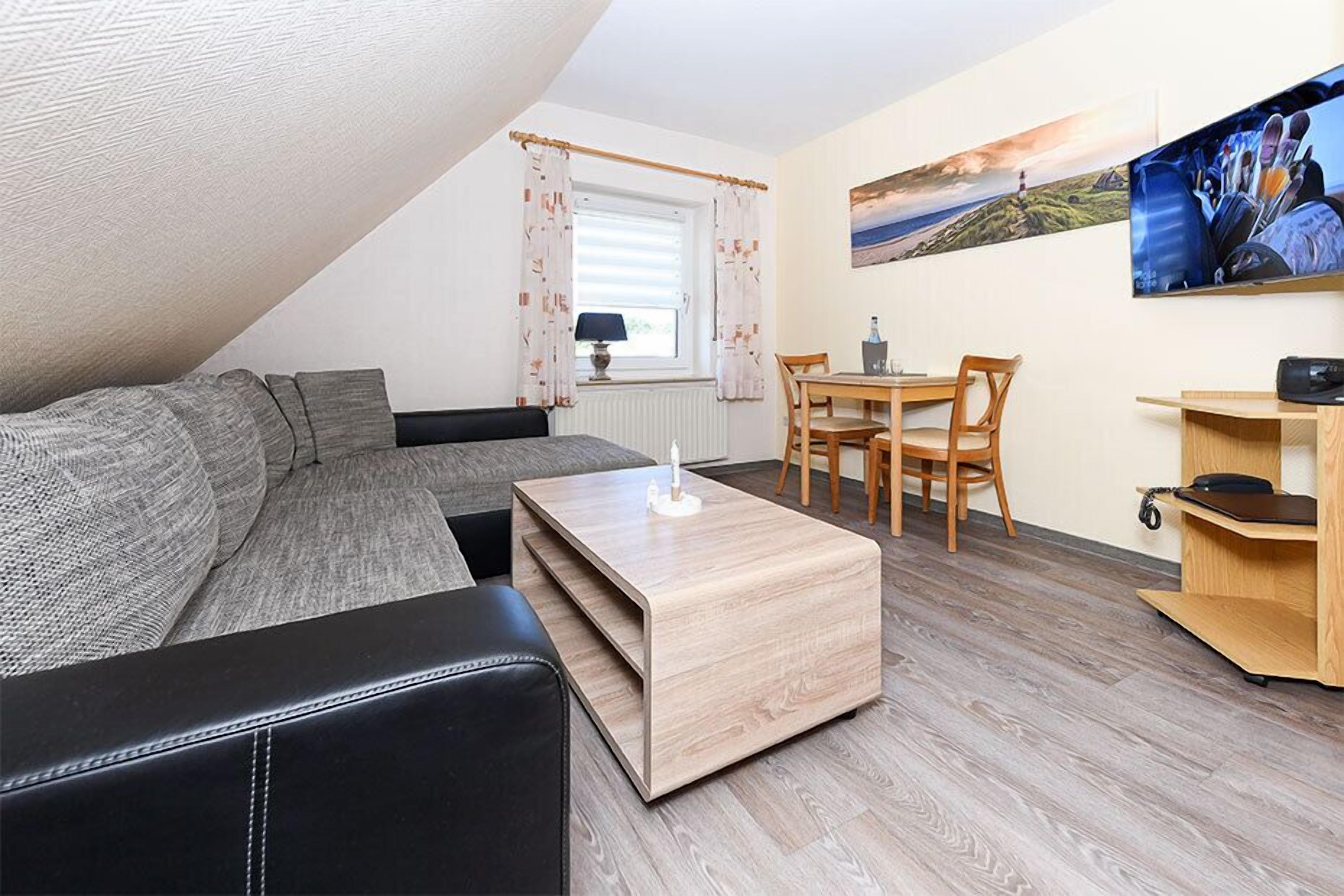 A compact living space with a sofa, a small dining table, a TV, and a wooden coffee table.