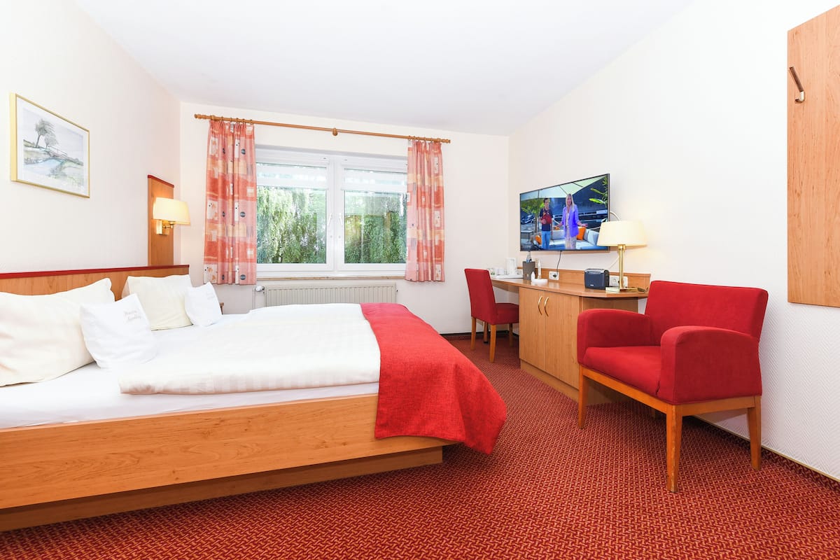 A hotel room with a bed, a desk, a chair, a TV, and a window with curtains.