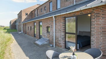 A brick building with a patio area featuring a round table and chairs, a small outdoor seating area, and a view of the surrounding landscape.
