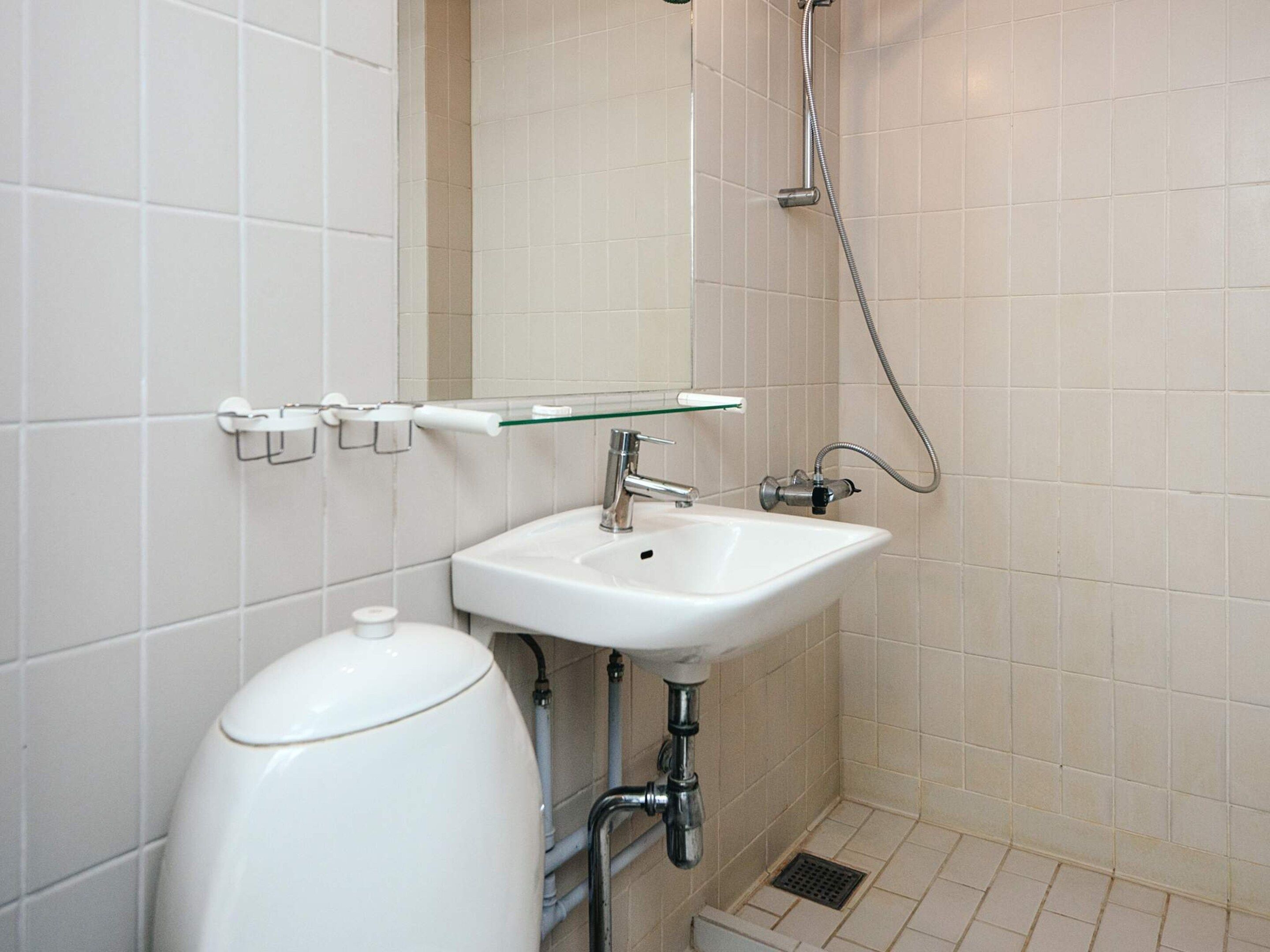 Un baño con un lavamanos blanco, repisa de vidrio, inodoro y ducha.