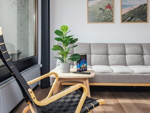 A modern living room with a sofa, a wooden chair, a potted plant, a small table, and a book. - 6 Person Holiday Park Home in Ulfborg (Ulfborg)