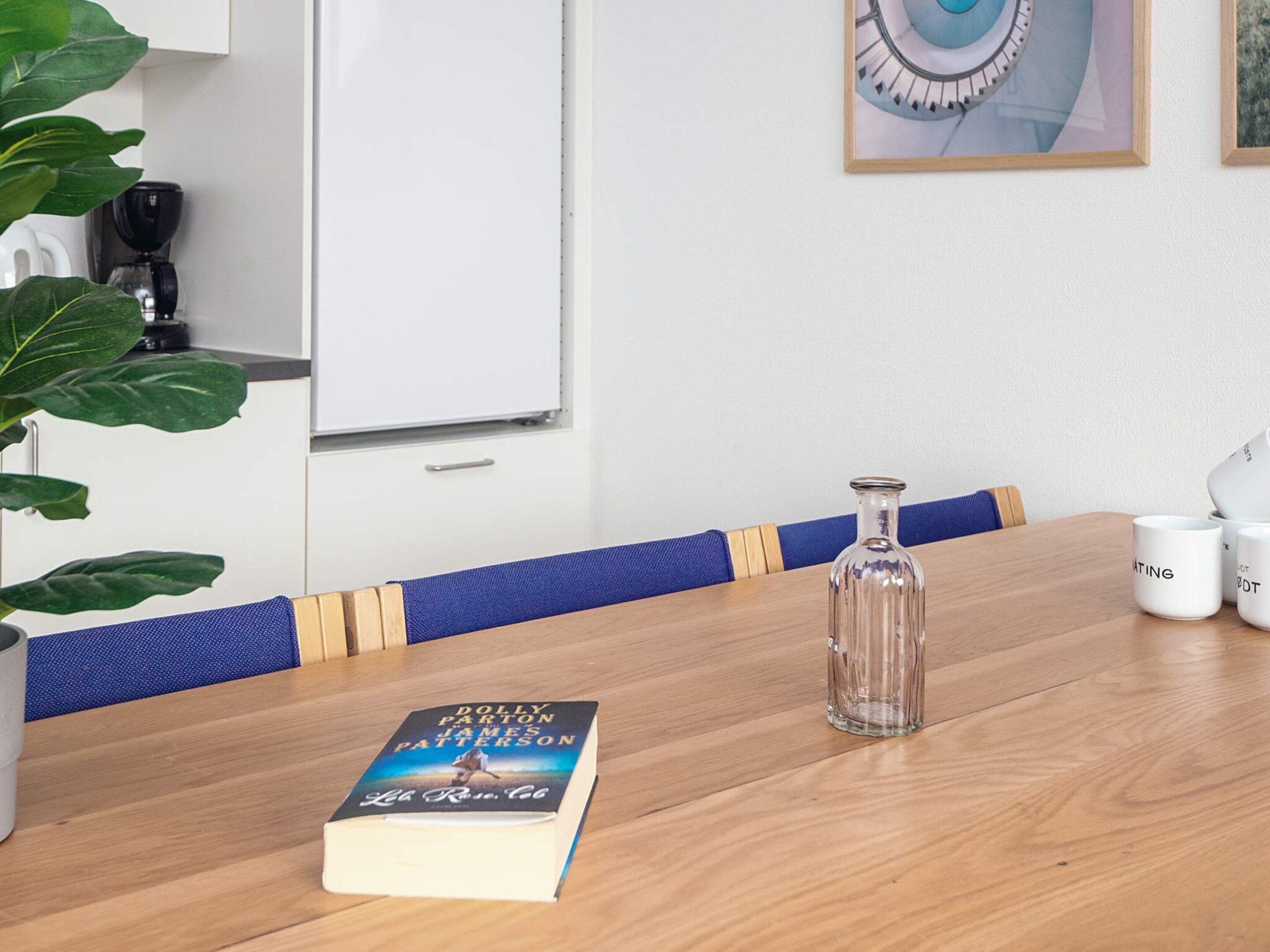 Una mesa de madera con un libro, una botella de vidrio y tazas blancas.