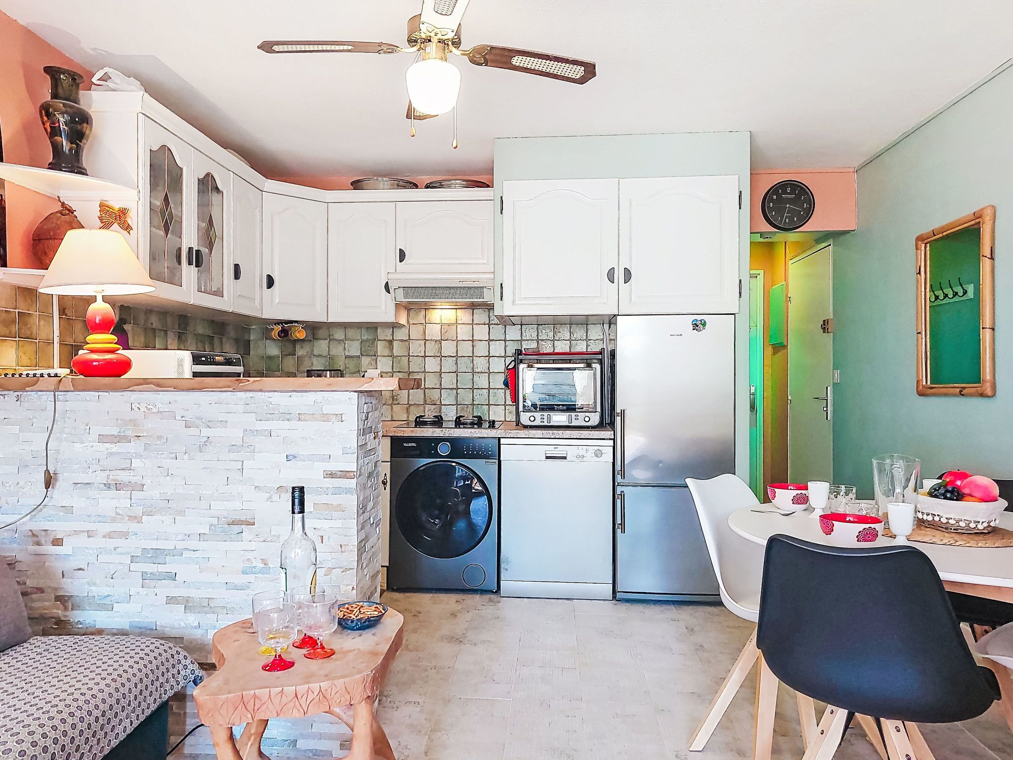 A compact kitchen with a washing machine, a refrigerator, a microwave, and a dining area with a table and chairs.