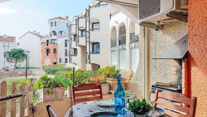 An outdoor dining area with a table set for two, surrounded by potted plants and a view of buildings. - Dominica by Interhome (Le Barcarès)