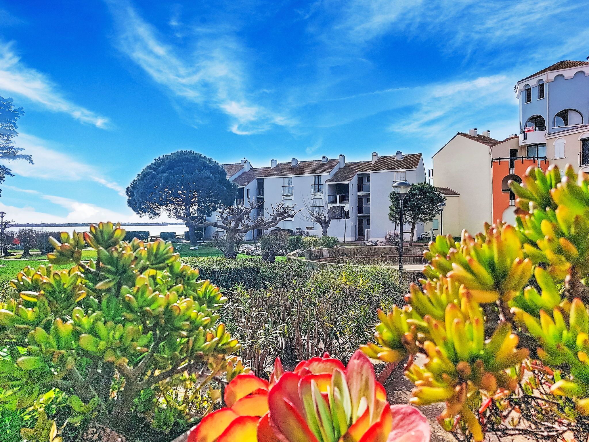 Un edificio costero con balcones, cielo despejado y un jardín con diversas plantas.