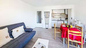 Ett modernt vardagsrum med en soffa, ett matbord och stolar, ett kök i bakgrunden och en taklampa.