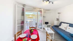En matplats med ett bord dukat för två personer, en soffa, en tv och en balkong med utsikt.