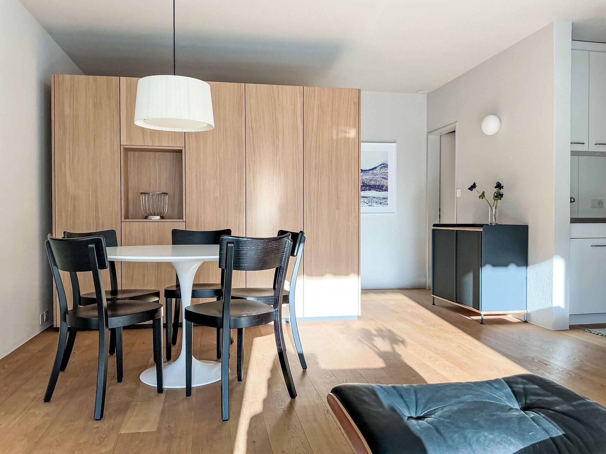 Une cuisine moderne avec des meubles en bois, une table à manger avec des chaises et un luminaire suspendu.