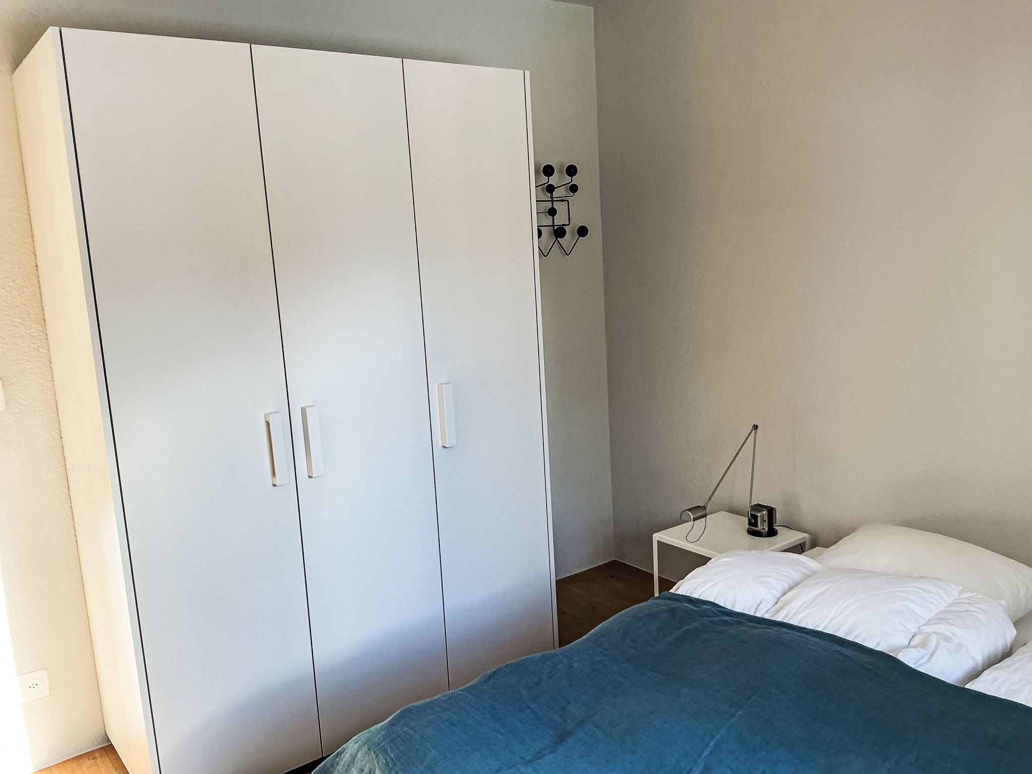 Camera da letto con un'ampia armadio, un comodino con una lampada e un letto con cuscini bianchi.