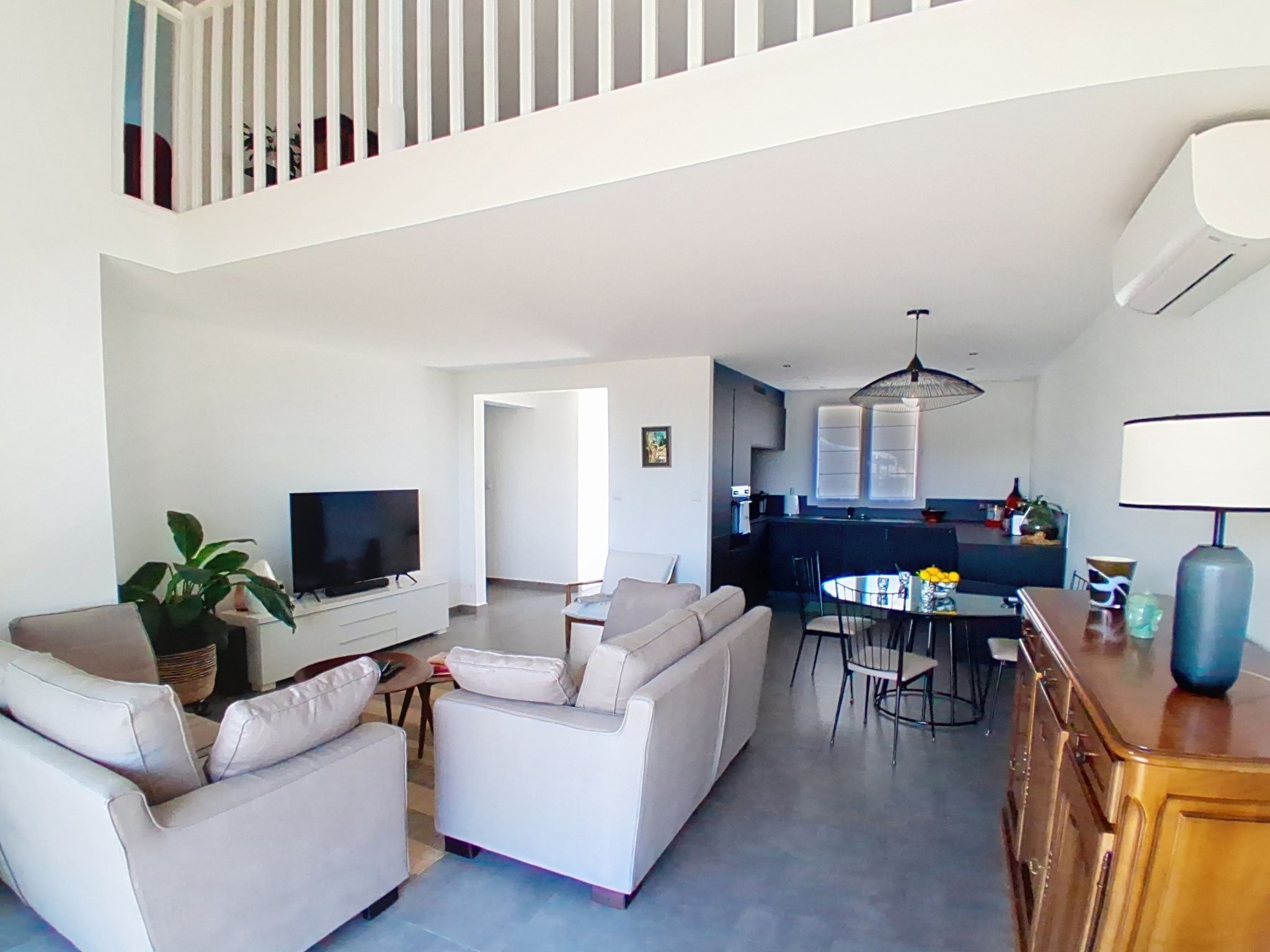 A modern living room with a sofa set, a TV, a dining table with chairs, and a kitchen area in the background.