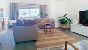 Un salon avec un canapé, une table basse, un téléviseur et une grande fenêtre avec des rideaux.