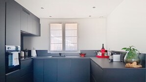 Une cuisine moderne avec des meubles de rangement aux couleurs foncées, une fenêtre et une petite plante posée sur le plan de travail.