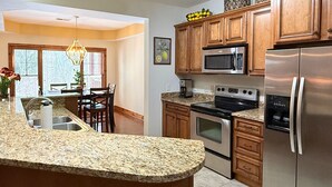 A kitchen with granite countertops, stainless steel appliances, wooden cabinets, and a dining area with a chandelier. - Beautiful Rustic Mountain Getaway at Elkmont (Banner Elk)