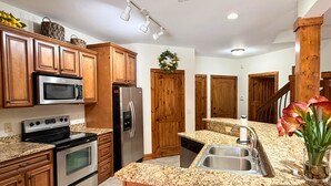 A kitchen with wooden cabinets, stainless steel appliances, granite countertops, a stainless steel sink, and a decorative plant. - Beautiful Rustic Mountain Getaway at Elkmont (Banner Elk)