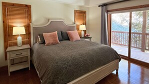 A bedroom with a large bed, wooden headboard, two bedside tables with lamps, a ceiling fan, and a view of a deck through a large window. - Beautiful Rustic Mountain Getaway at Elkmont (Banner Elk)