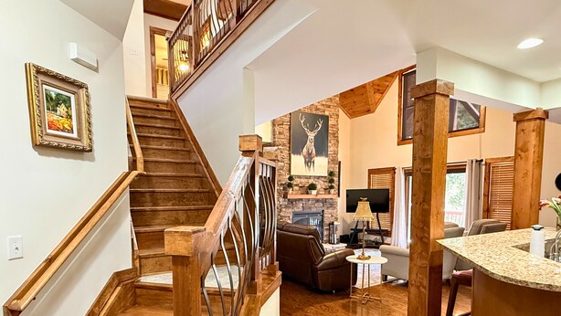 A spacious living area with a wooden staircase, a fireplace, a stone wall, and a large TV. - Beautiful Rustic Mountain Getaway at Elkmont (Banner Elk)