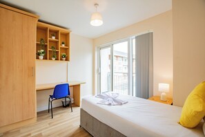 Ein Hotelzimmer mit Bett, Schreibtisch, Stuhl, Kleiderschrank, Fenster und Nachttischlampe.