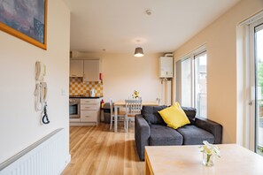 Ein modernes Wohnzimmer mit einer Couch, einem Esstisch und einer Küchenzeile im Hintergrund.