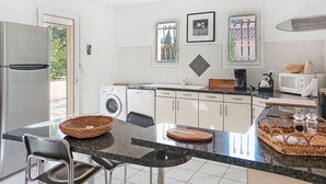A modern kitchen with a refrigerator, washing machine, microwave, and a dining area with chairs and a table. - Villa Brouilla by Interhome (Brouilla)