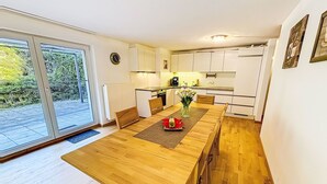 A modern kitchen with white cabinets, a dining table with chairs, and a view through the glass door to the outside. - Happy Living by Interhome (Vandans)