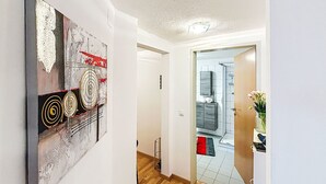 A hallway with a modern abstract painting, a wooden floor, and a view into a bathroom with a mirror and a sink. - Happy Living by Interhome (Vandans)