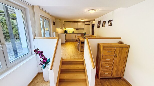 A staircase leading to a kitchen with wooden flooring, a dining area, and a view of greenery outside. - Happy Living by Interhome (Vandans)