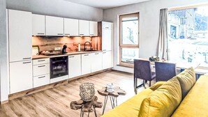 Une cuisine moderne avec des meubles blancs, un coin repas doté d’un canapé jaune et une grande fenêtre offrant une belle vue.