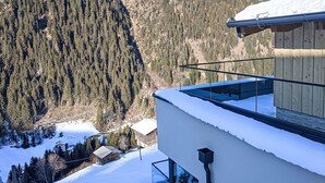 Un bâtiment moderne doté d’un balcon en verre offrant une vue sur un paysage montagneux enneigé.